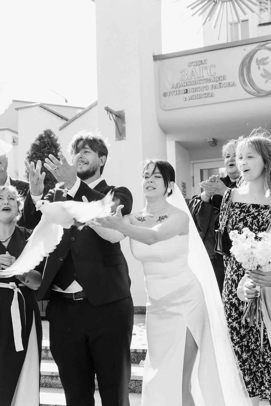 A black and white image of a bride and groom releasing a dove, a funny wedding photo moment with cheering guests.