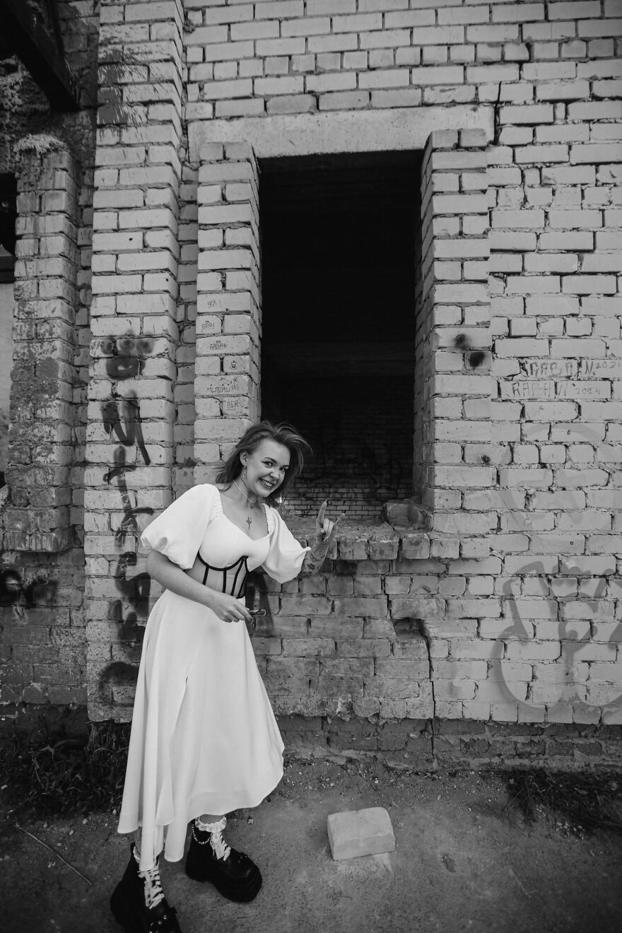 A smiling bride in a white dress and boots making a gesture, posing for a funny wedding photo.