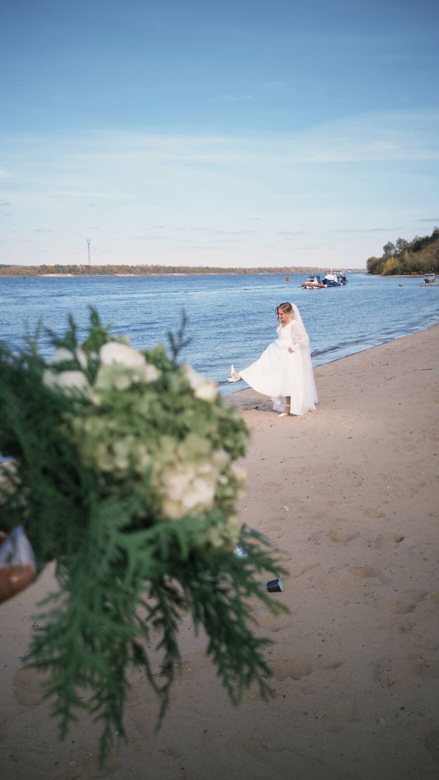A bride with a wedding dress on a beach near water, enjoying a funny wedding photo.