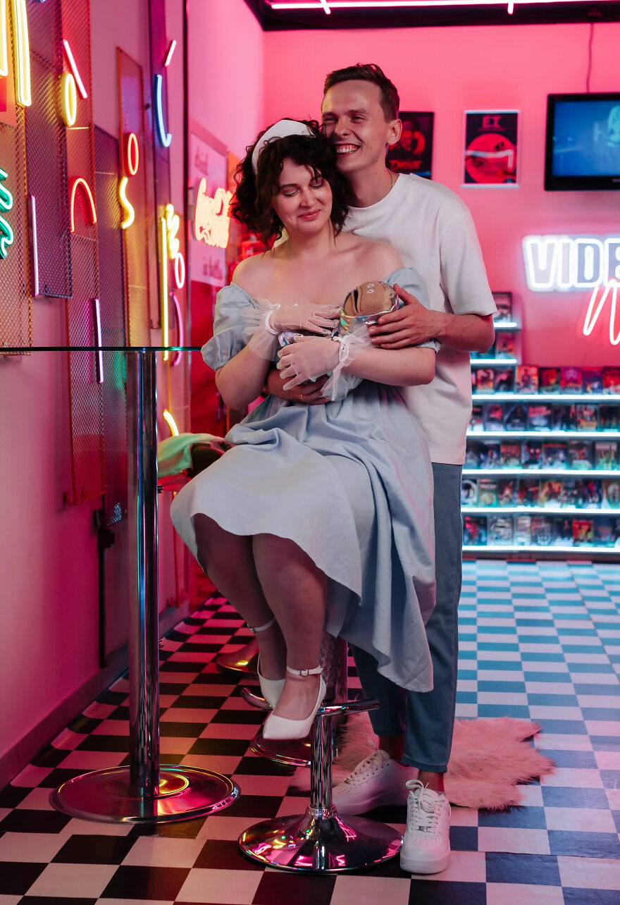 A couple posing in a retro-themed room with neon lights, a unique and funny wedding photo, with the bride holding a small object.