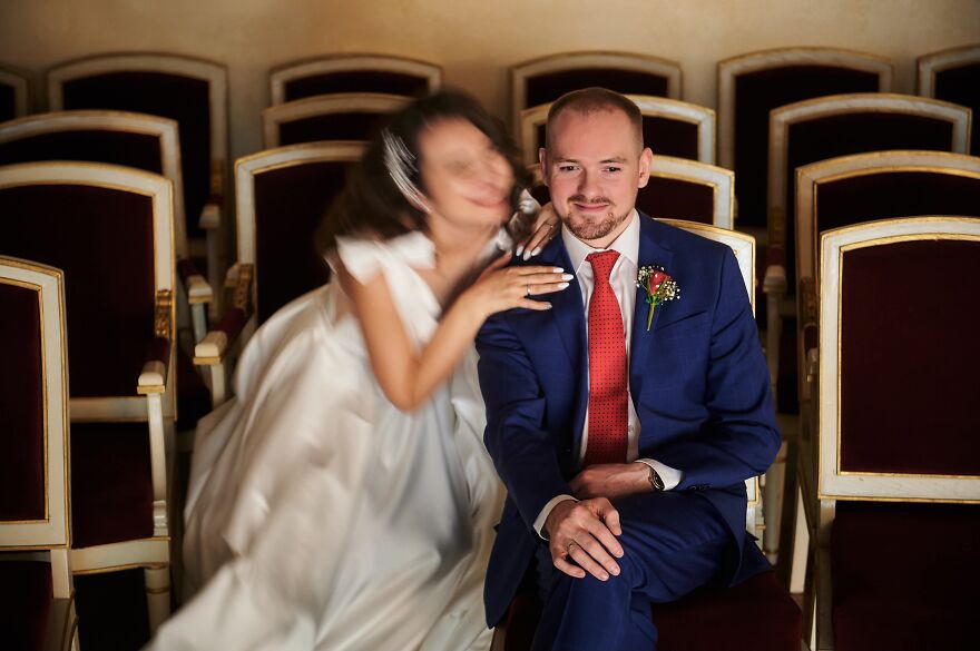 A blurry bride embracing a focused groom in a blue suit with a red tie, capturing a funny wedding photo.