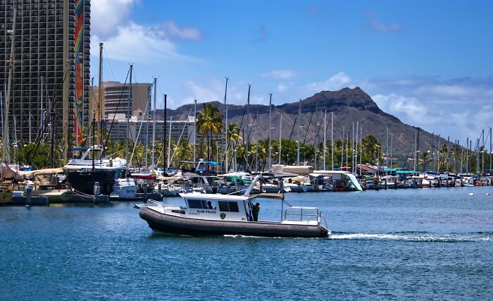 A police boat in a harbor with disturbing tall buildings and a scary mountain in the background.