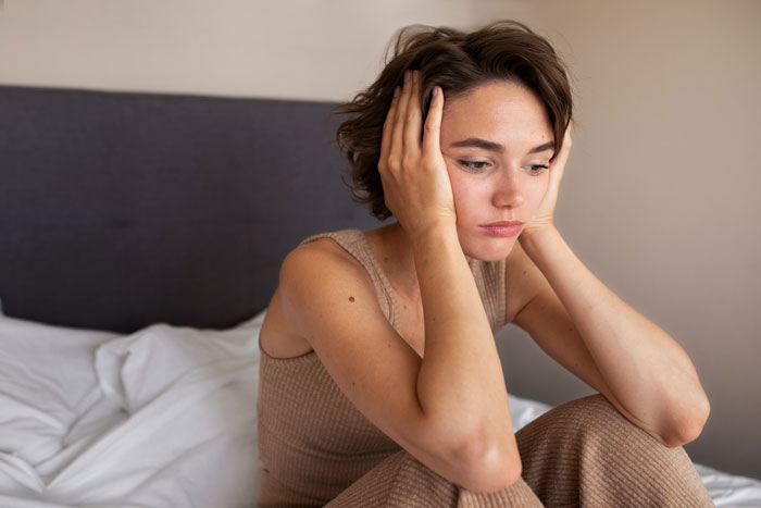 A young woman looking anxious, sitting on a bed, concerned about a sibling's service dog being banned from wedding.