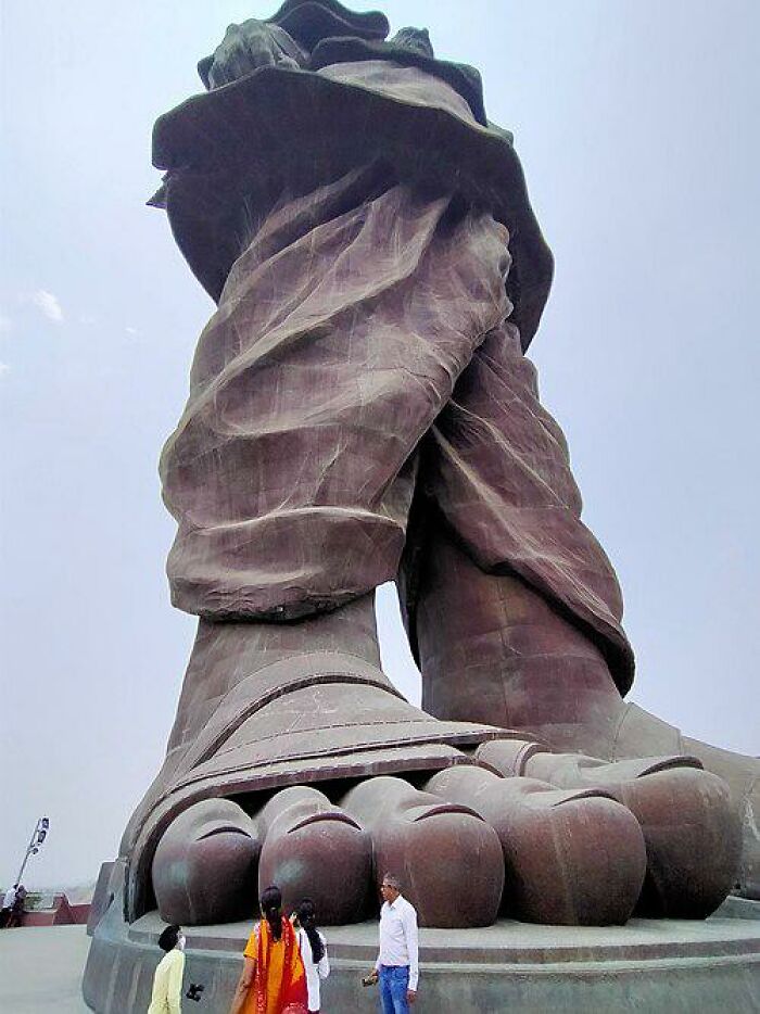 The colossal feet of a giant statue, dwarfing people standing near its base, highlighting its true scale in size comparisons.