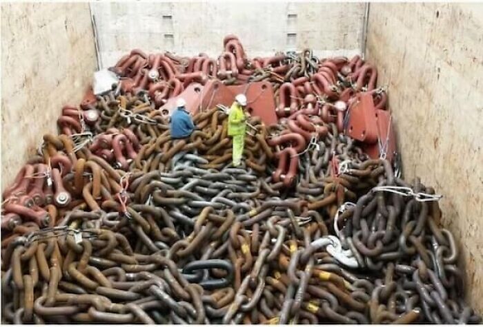 Two workers standing amidst an enormous pile of anchor chains, highlighting the true scale of industrial components.