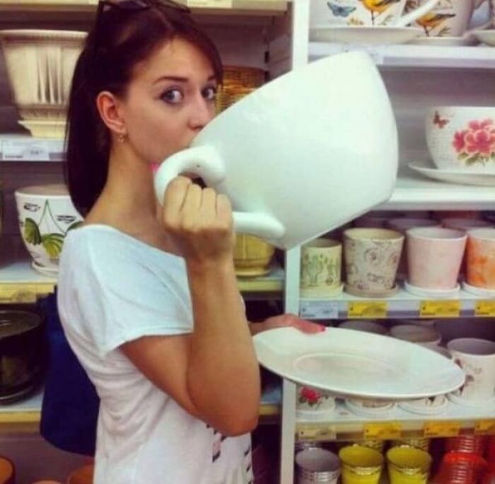 A woman pretending to drink from an oversized teacup, a fun size comparison highlighting the true scale of novelty items.