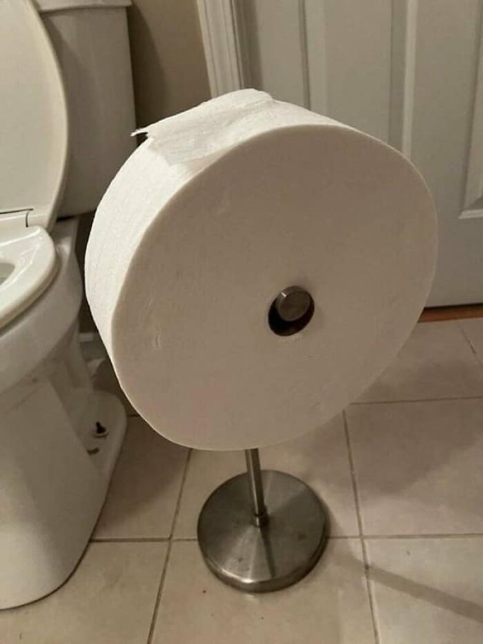 A massive toilet paper roll on a holder, showing its true scale next to a standard toilet for size comparisons.