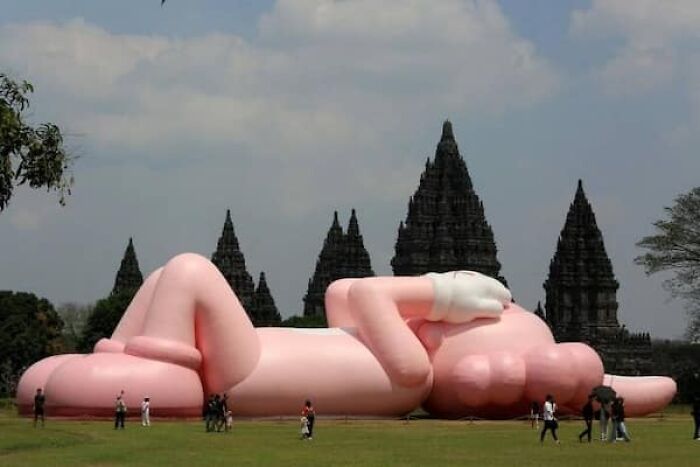 A huge inflatable human figure lying on the grass next to ancient temples, demonstrating its true scale.