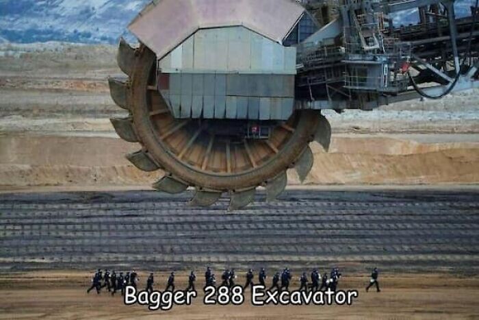 A group of people walking under the Bagger 288 excavator, highlighting the true scale of the machine.