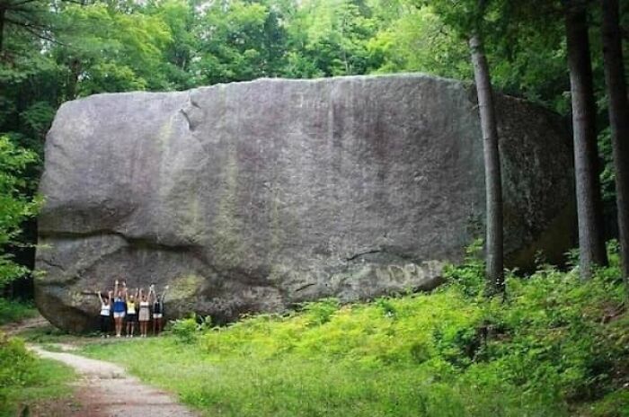 A group of people standing next to a massive boulder, illustrating the true scale of the rock.