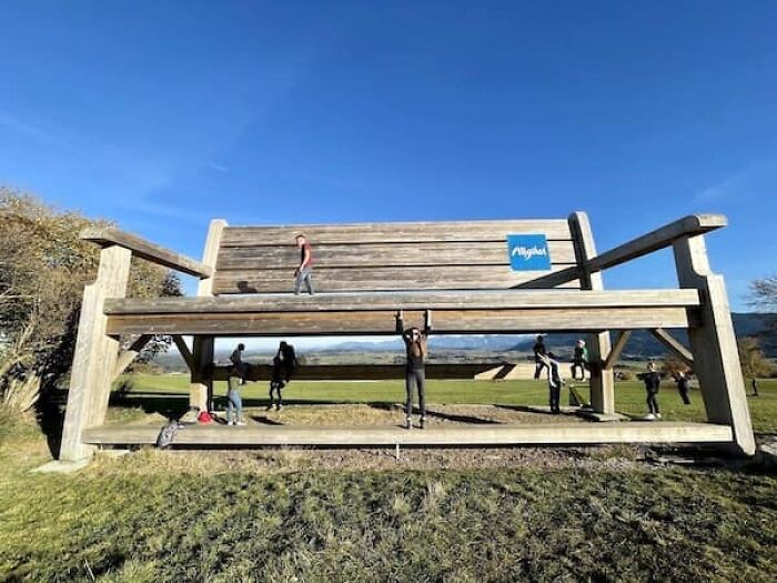 A massive wooden bench with people climbing on it, showing the true scale of things.