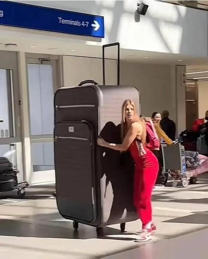 Woman at an airport struggling to move a massive suitcase, demonstrating size comparisons for luggage.