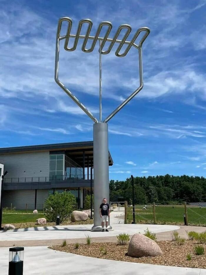 Man standing next to a giant potato masher, showcasing a size comparison of the kitchen tool.