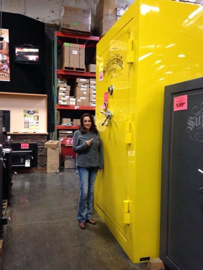 A woman standing next to a massive yellow safe, highlighting the impressive scale of the object.