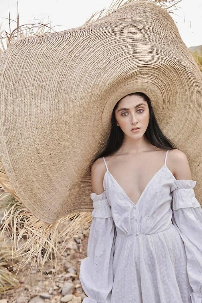 Woman wearing an oversized straw hat, showcasing the true scale of the accessory.