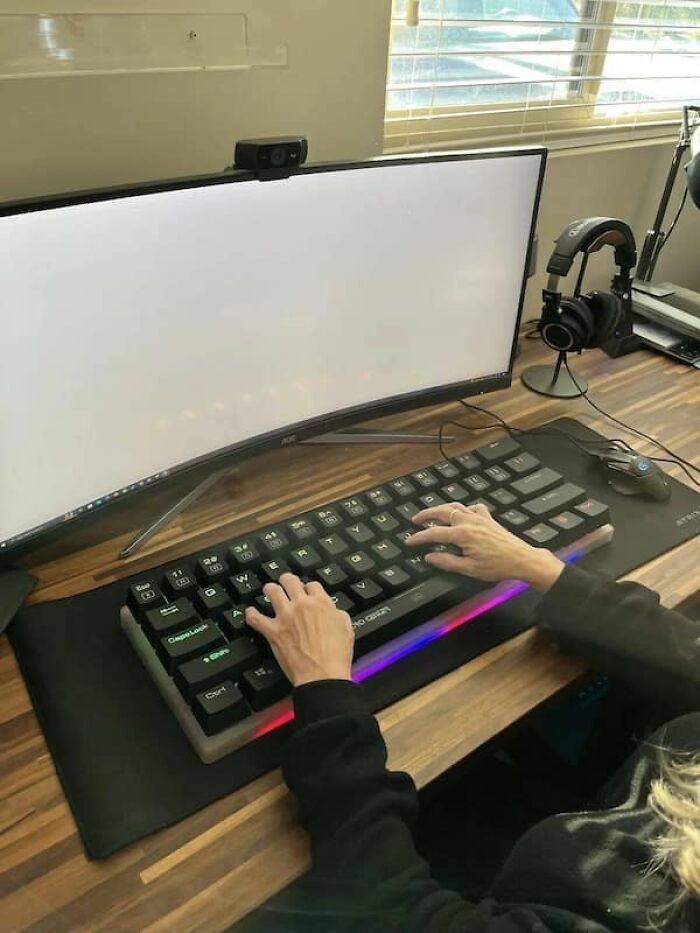 Tiny hands on a large gaming keyboard with a curved monitor, for a size comparison.
