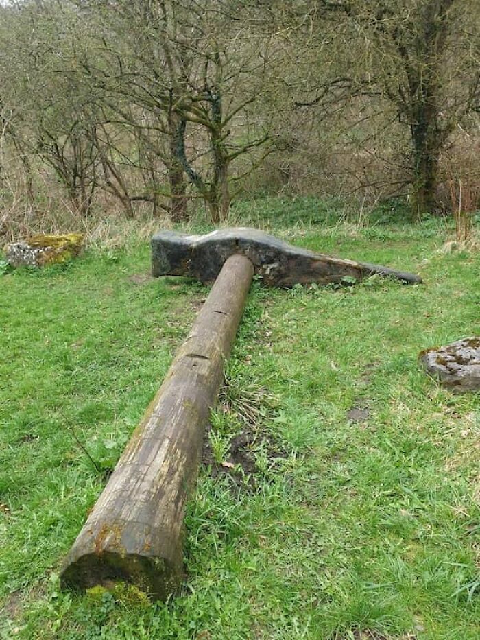 An enormous hammer with a wooden handle lying in a grassy field, demonstrating its true scale.