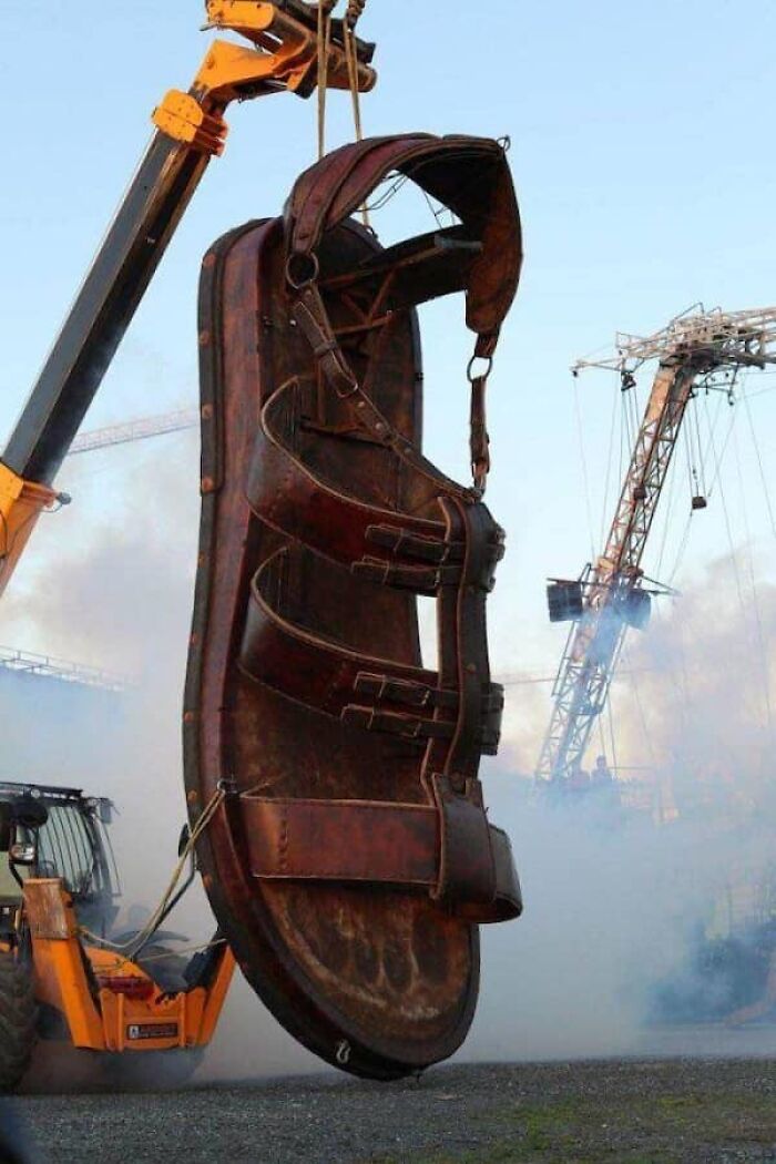 Massive sandal sculpture lifted by a crane, showing the true scale of the footwear.