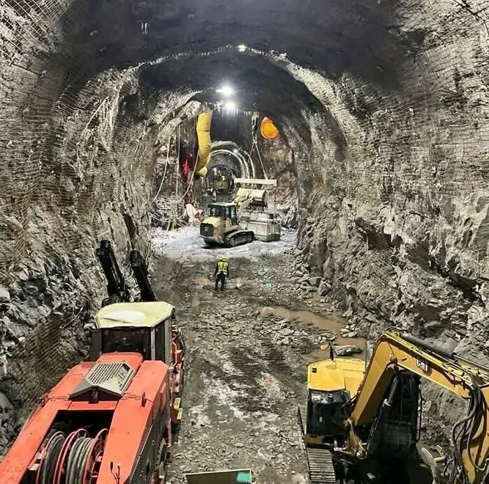 Large machinery and a worker in a massive underground tunnel, showing the true scale of the excavation project.