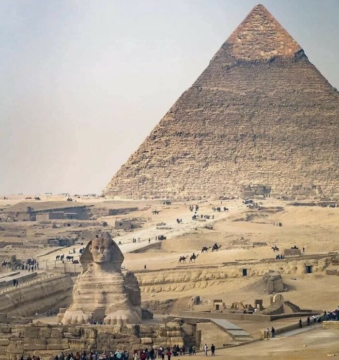 The Great Sphinx and a pyramid in Egypt, with people and camels in the foreground for size comparisons.