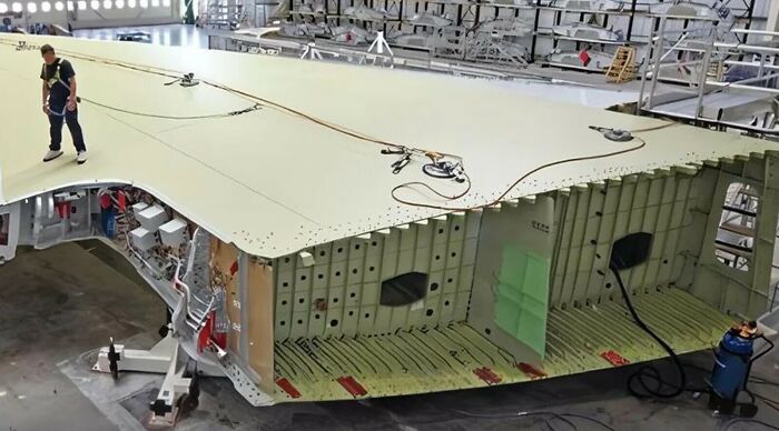 A worker standing on an enormous airplane wing during construction, highlighting the true scale of aircraft manufacturing.