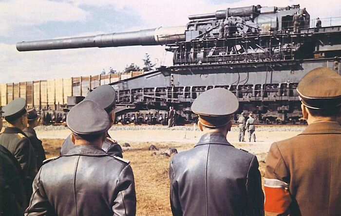 Soldiers observing the true scale of a massive railway gun, highlighting its impressive size comparison.
