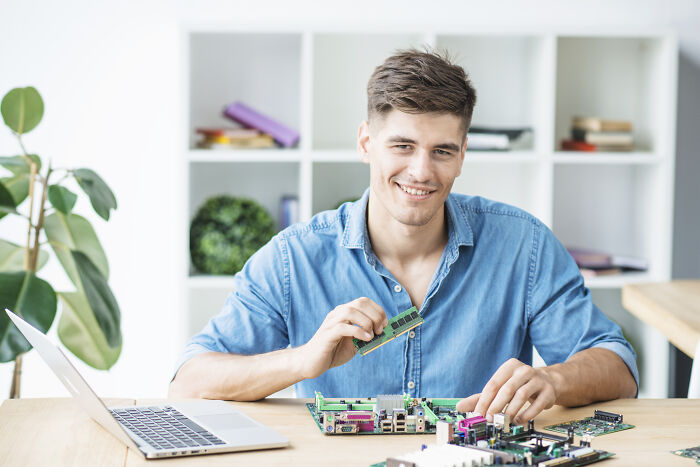 Smiling man inserting RAM into a motherboard, representing unpopular industries that make millions.