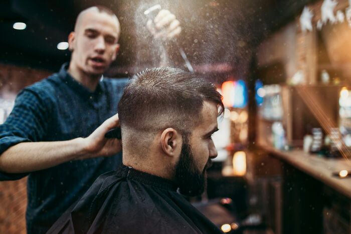 A barber sprays water on a client's hair before a haircut; a potentially socially awkward situation.