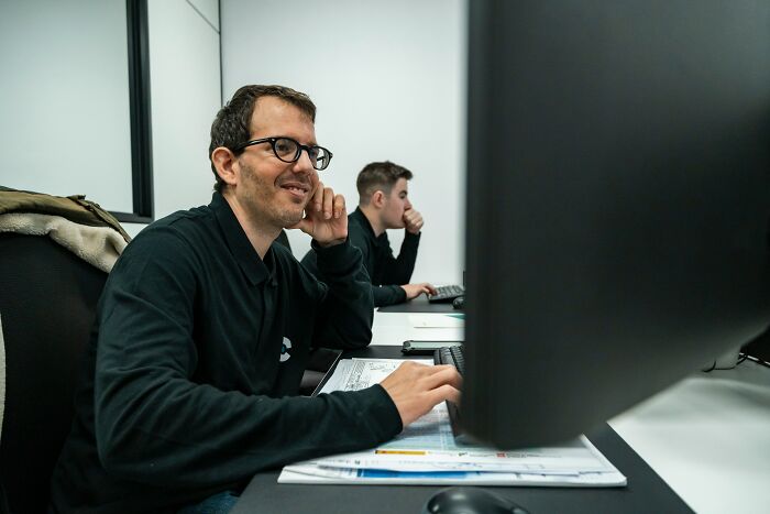 A man in glasses smiles while working on a computer; a socially awkward moment, perhaps.