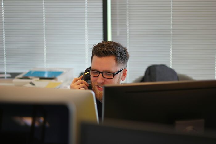 A socially awkward man on the phone at his desk, showcasing a cringe moment.