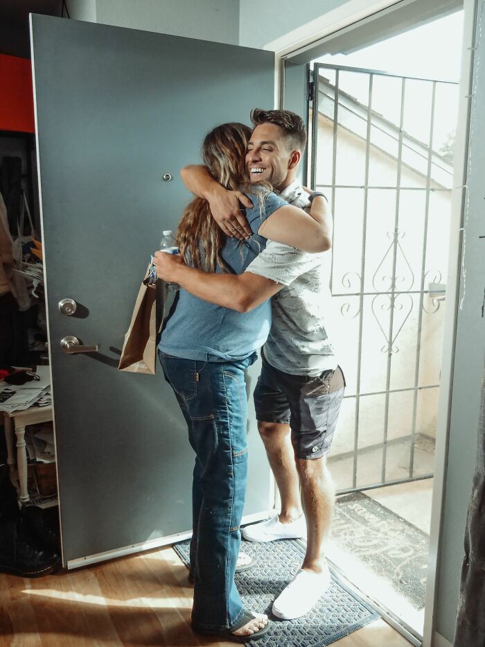 A socially awkward man enthusiastically hugging a woman at the doorway, creating a cringe moment.
