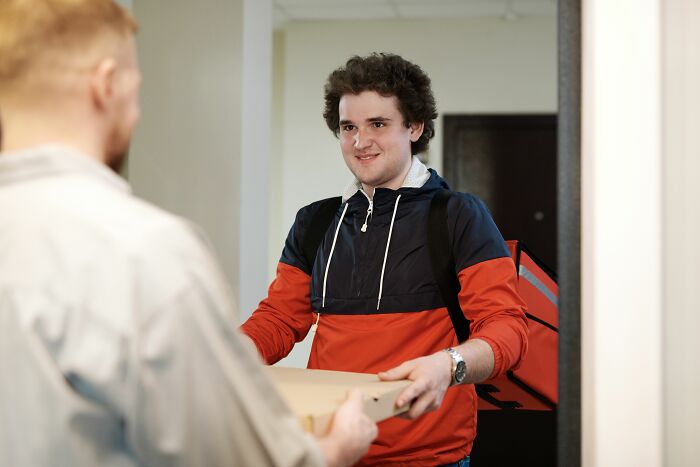 A delivery person, appearing socially awkward, handing over a package, recalling cringe moments.