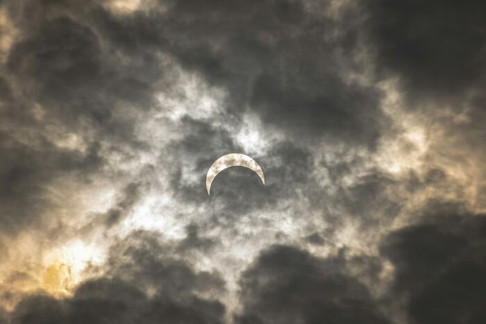 A partial solar eclipse visible through dark, dramatic clouds, emphasizing varied viewing conditions. A partial solar eclipse visible through dark, dramatic clouds, emphasizing varied viewing conditions.