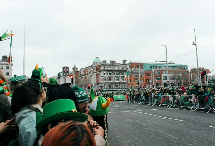 A crowd of people in green hats lining a city street, ready for a parade related to unsolved mysteries.