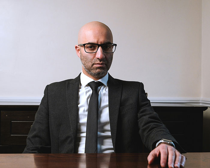 A divorce lawyer in glasses and a suit, sitting, reflecting on instant karma cases.