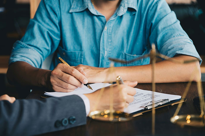 Hands signing divorce papers with a scale of justice, representing the legal process and instant karma.
