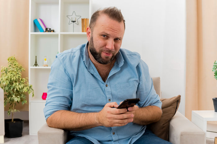 A man with a beard, possibly the step-dad, holding a phone in a room, related to the spy camera issue. A man with a beard, possibly the step-dad, holding a phone in a room, related to the spy camera issue.