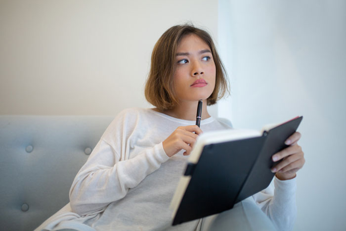 Woman pondering with a notebook, reflecting on the spy camera room and step dad situation. Woman pondering with a notebook, reflecting on the spy camera room and step dad situation.