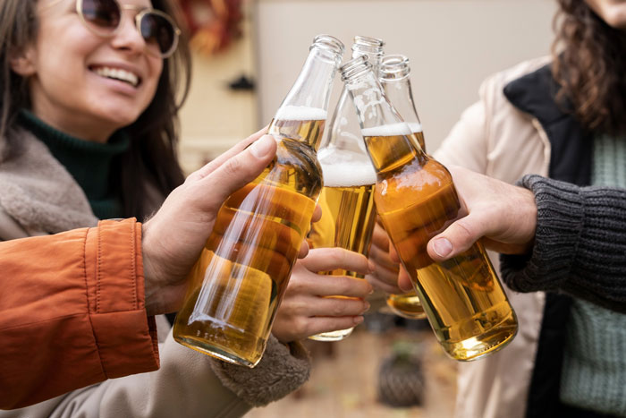 Friends toasting beer bottles, discussing the age to give up beer for their nervous system.