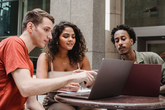 Three students engaged in group work, collaborating on laptops, a contrast to the student refusing group work and facing a hard fail. Three students engaged in group work, collaborating on laptops, a contrast to the student refusing group work and facing a hard fail.