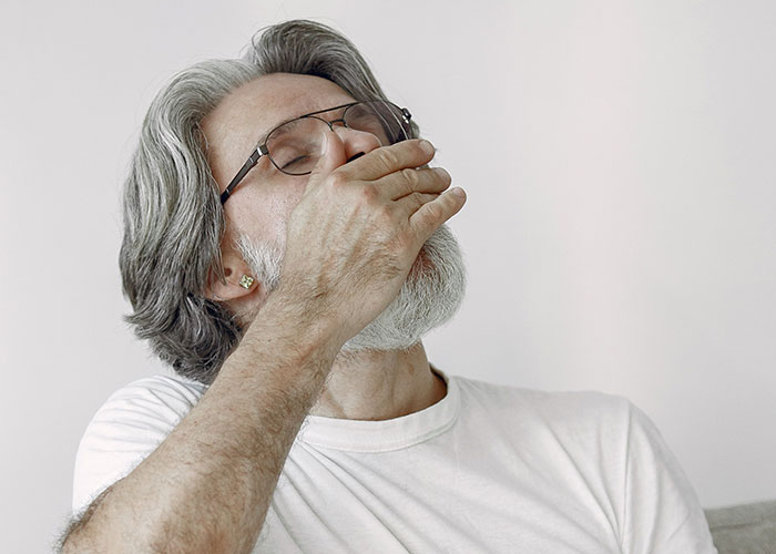 A man with grey hair and a beard covers his mouth, demonstrating human body facts.