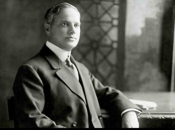 Black and white portrait of a man in a suit, sitting at a desk, sharing coolest history facts.