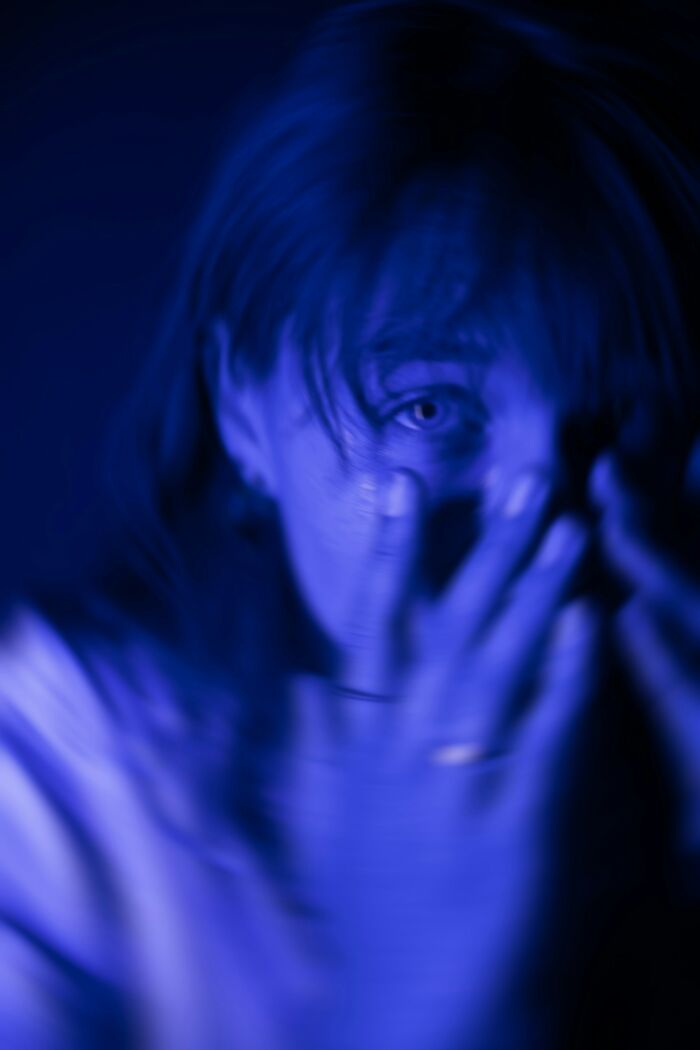 A blurred, blue-toned image of a person with one eye visible, their hands covering their face, instincts telling them to get away from creeps.