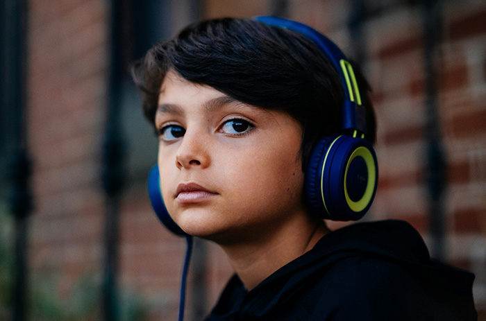 A young boy with dark hair and blue headphones looks intently at the camera, learning a lesson. A young boy with dark hair and blue headphones looks intently at the camera, learning a lesson.