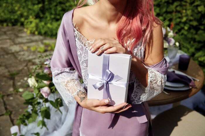 A person with pink hair holding a wedding gift, regretting the money spent.