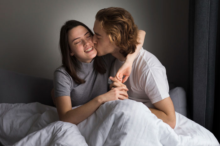 A man kissing a woman on the cheek in bed. This image represents a quiet love life in a relationship.