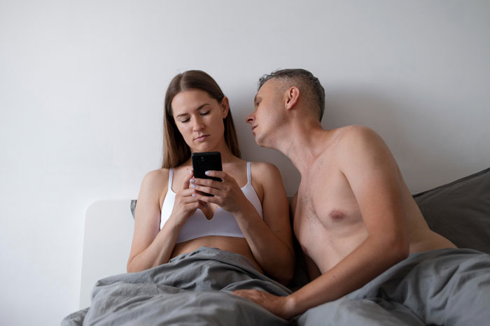 Couple in bed showing love life going quiet with woman distracted by phone