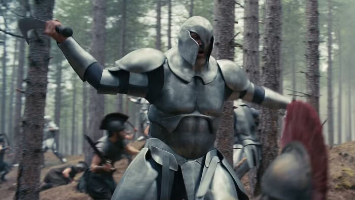 Christopher Nolan's Odyssey: A warrior in full armor swinging a sword in a forest, a new photo.