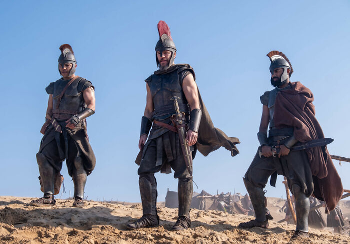 Three men in ancient warrior costumes standing on a sandy set. Christopher Nolan's bizarre rules spark backlash on set. Three men in ancient warrior costumes standing on a sandy set. Christopher Nolan's bizarre rules spark backlash on set.