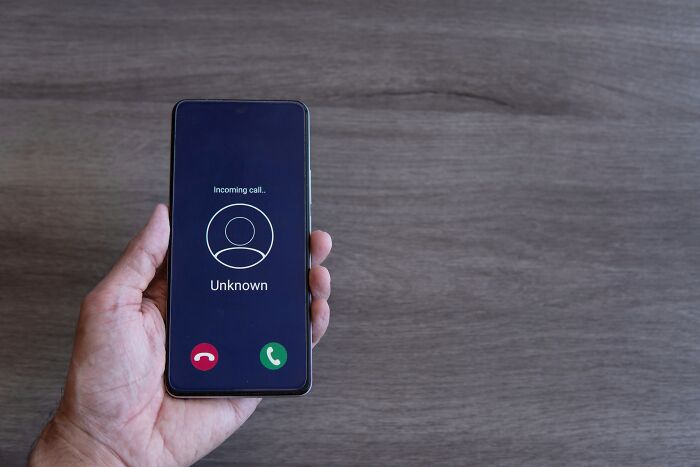 A hand holding a smartphone showing an incoming call from an unknown number, hinting at internet's creepy unsolved mysteries.